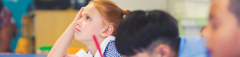 Photo of young girl looking up from her work in class
